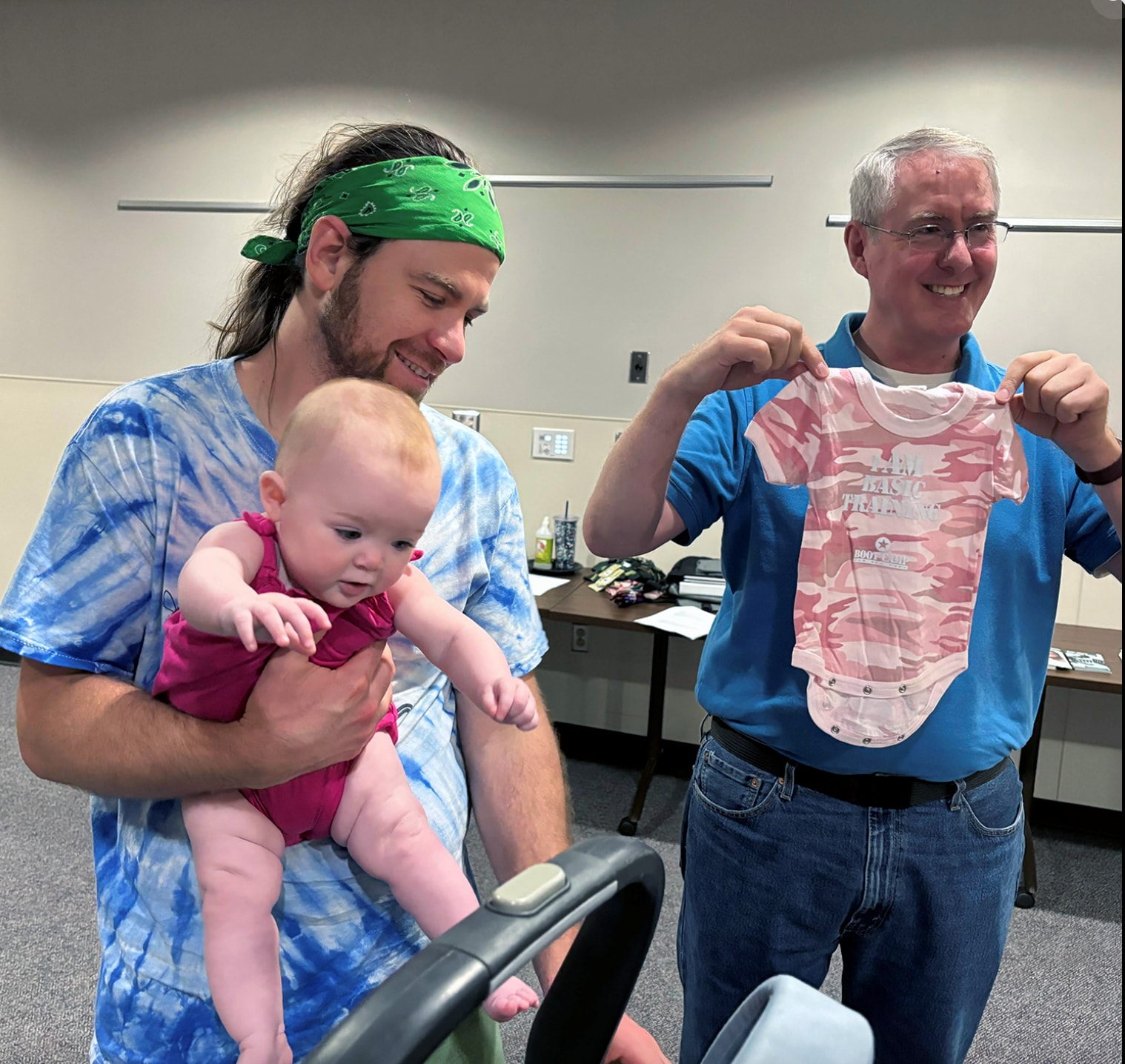 Charlie Bryan, longtime board member of Dads of Douglas County, gives a onesie to Cain Mathis and his daughter in July 2024.