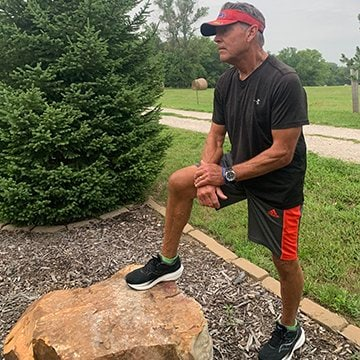Scot Hoffman wears running gear and stands with his foot up on a rock